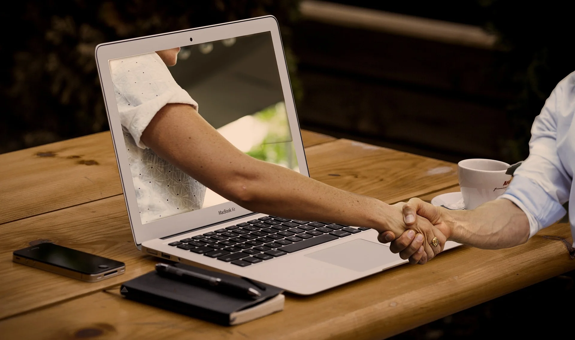 Two people shaking hands through a laptop screen, symbolizing a virtual agreement on Facebook Marketplace.