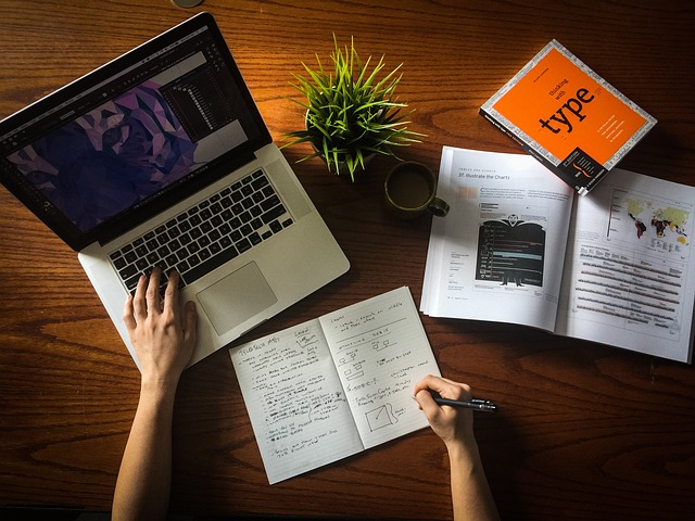 A workspace showing a laptop, a notebook, and a book about type design. This image symbolizes the strategic thinking and planning required for effective B2B and B2C digital marketing.