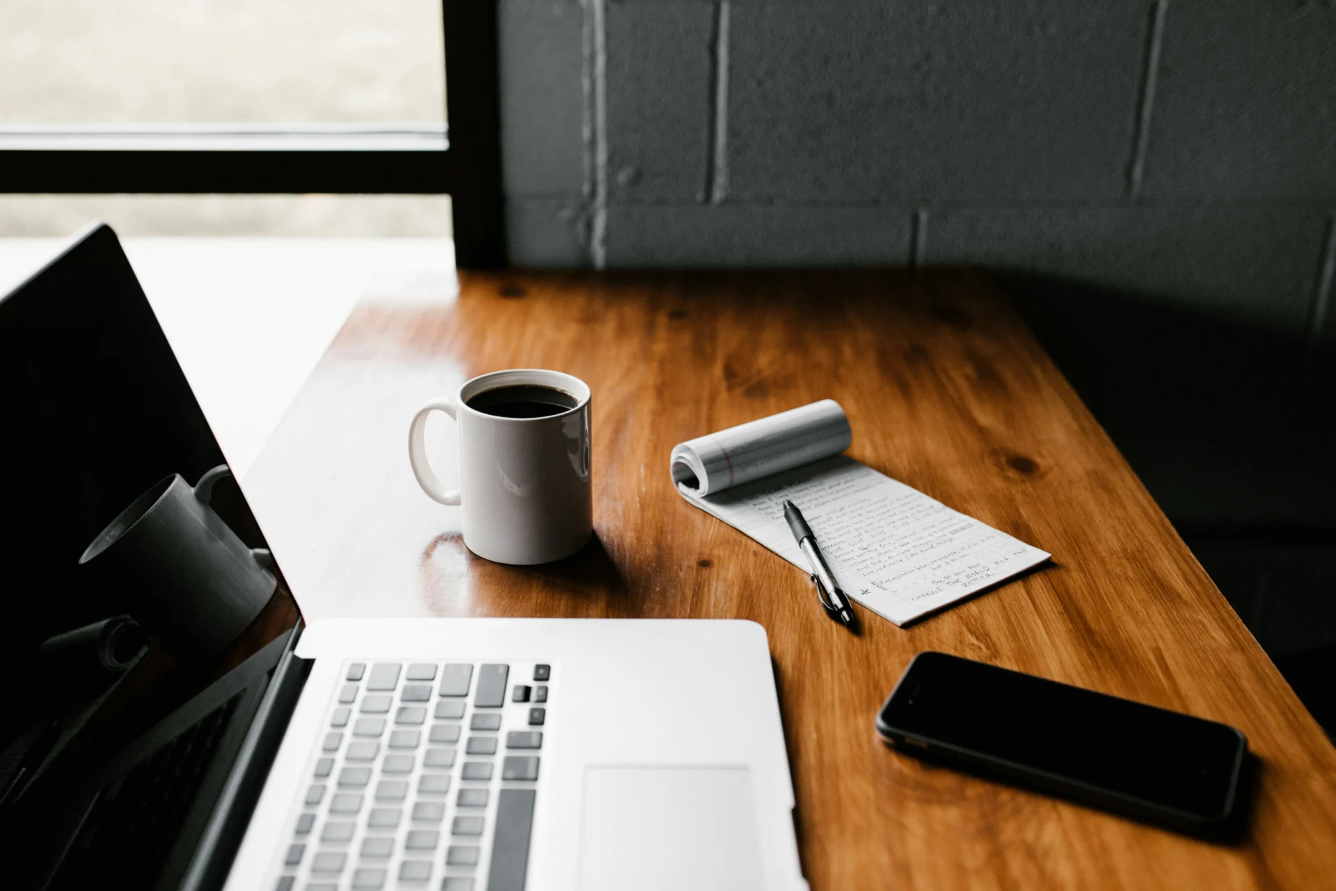 Laptop, coffee mug, notepad, and phone on a desk, suggesting content creation and guest blogging.