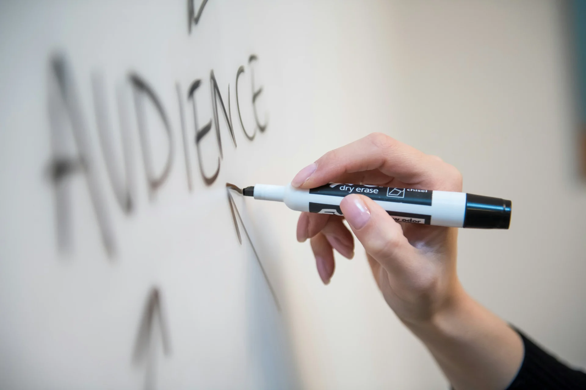 Hand writing "AUDIENCE" on a whiteboard with a dry erase marker, illustrating the concept of audience segmentation.