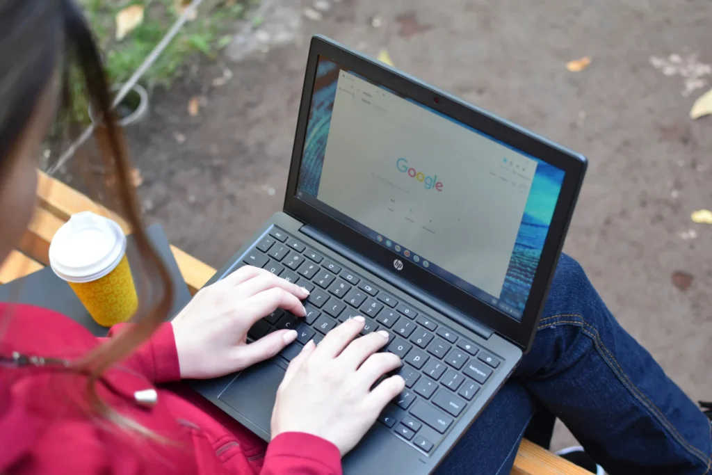 Woman typing on a laptop with a Google search page on the screen, sitting outdoors, symbolizing long tail keyword research.