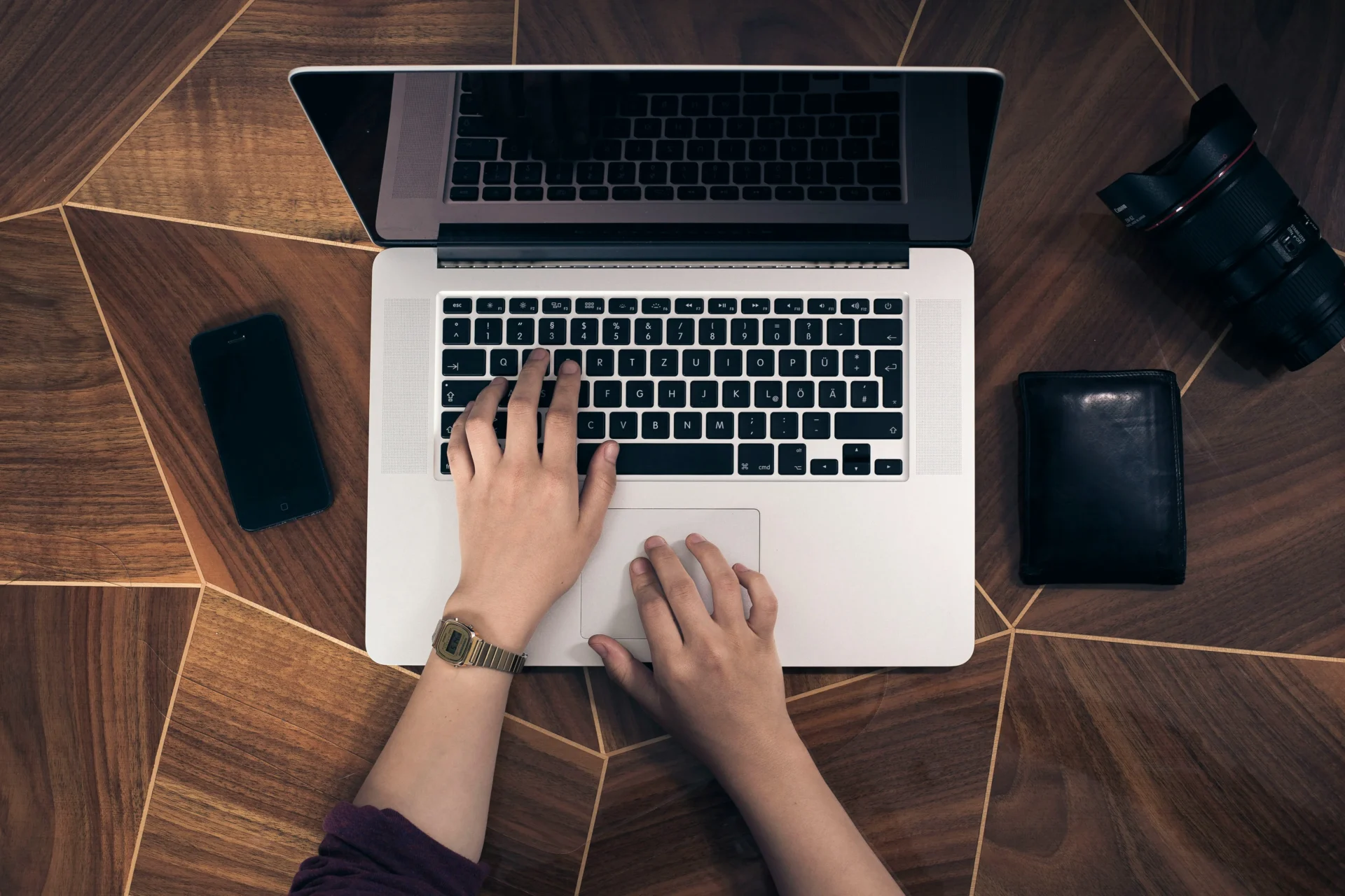 Hands typing on a laptop with a smartphone, wallet, and camera lens nearby, suggesting work related to personalizing automated marketing messages.