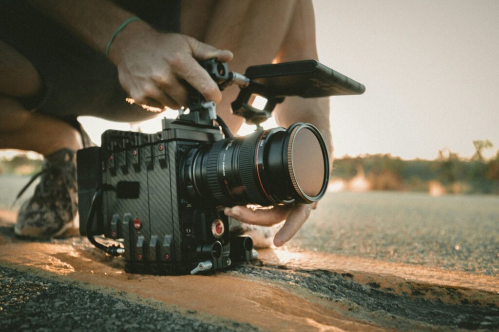 Hands adjusting a professional cinema camera on a tripod outdoors at sunset.