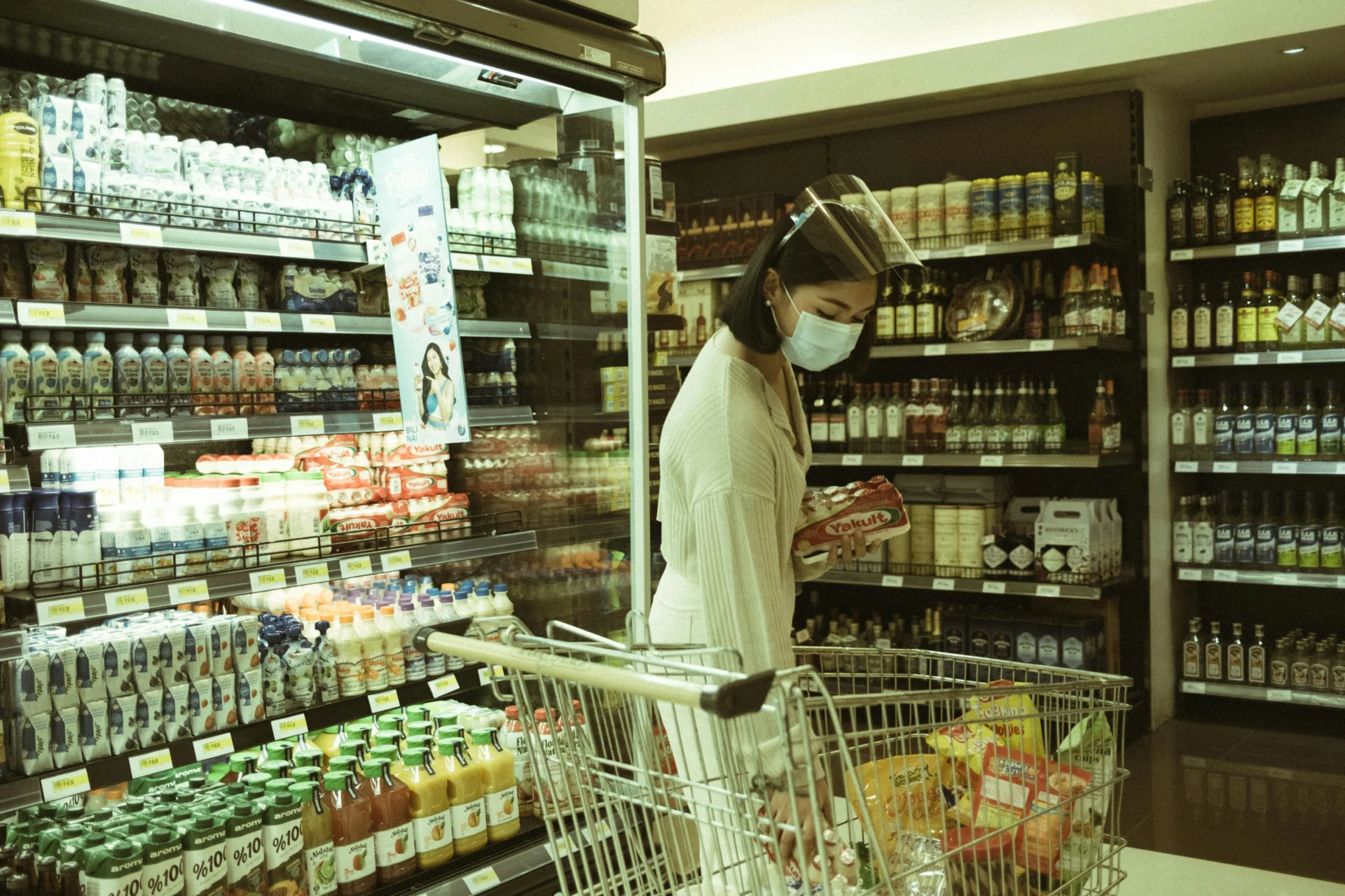Customer wearing a face shield and mask shopping for Yakult in a supermarket, reflecting customer experience in retail settings.