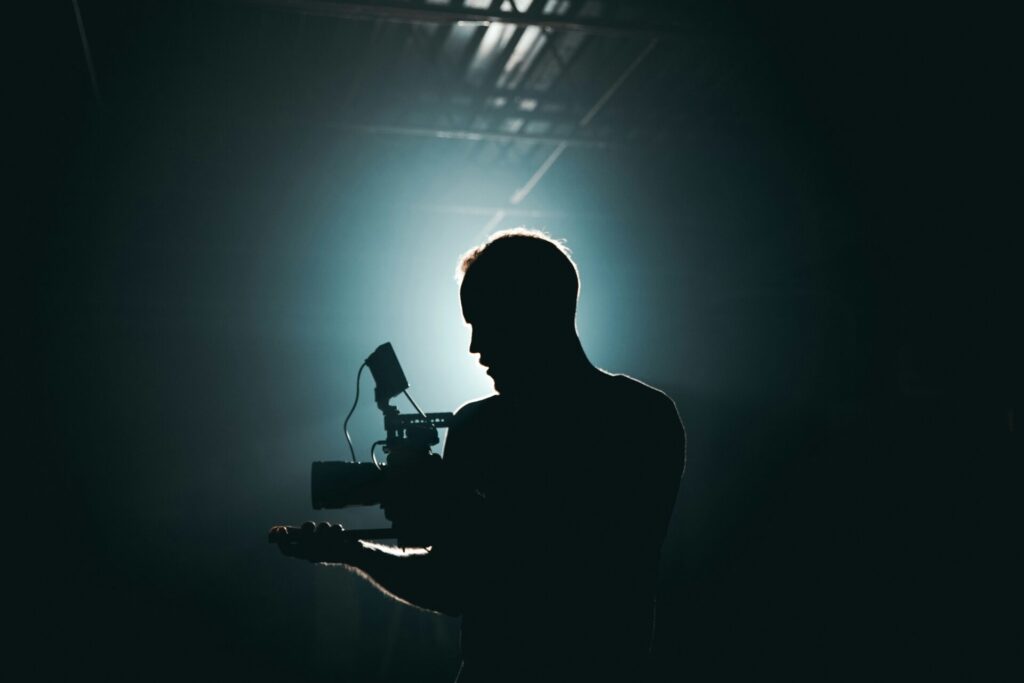 Silhouette of a filmmaker operating a camera in a dimly lit studio setting for visual storytelling services.