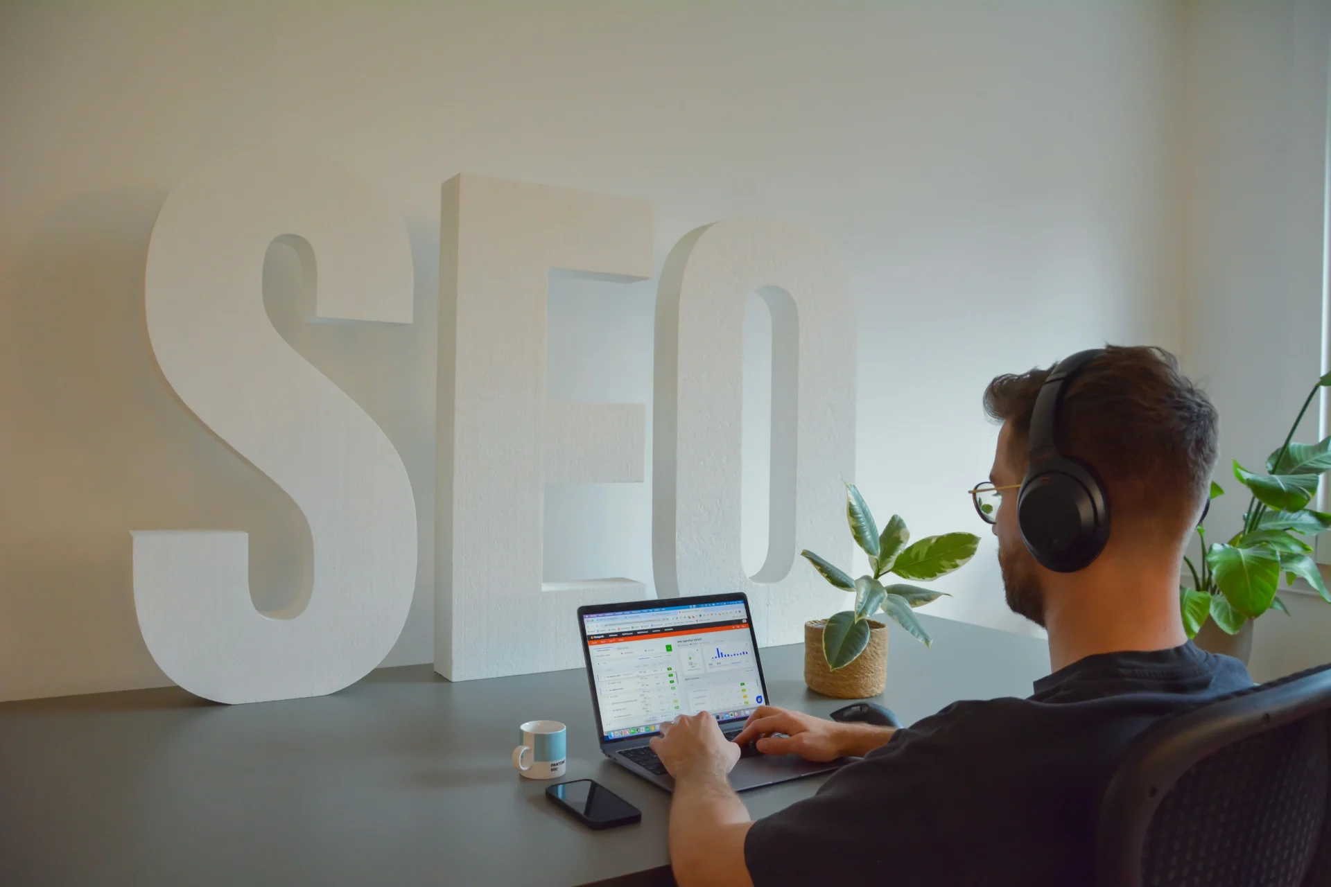 Person wearing headphones working on a laptop in front of large "SEO" letters, illustrating the concept of AI driven SEO strategies.