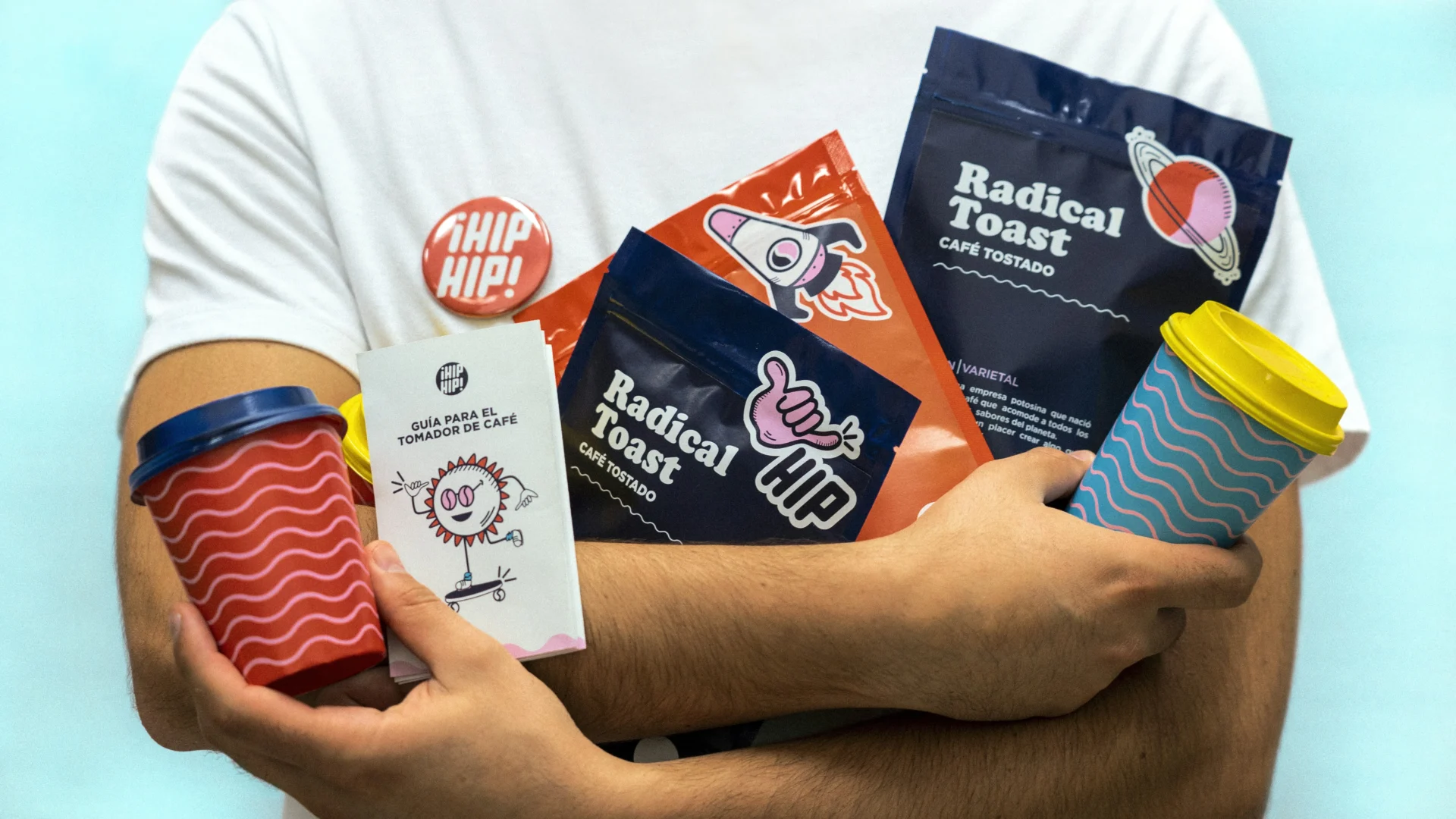 Close-up of hands holding various coffee product packaging including bags of roasted coffee, a coffee guide booklet, and reusable coffee cups, showcasing food and beverage packaging design.