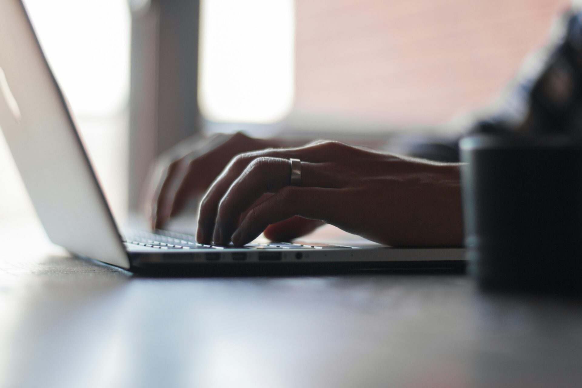 Hands typing on a laptop with a search page visible, smartphone and office phone nearby.