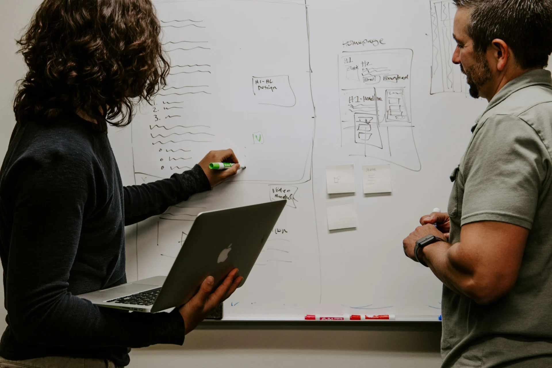 Two people collaborating on a whiteboard with diagrams and notes, discussing strategies for B2B search engine marketing.