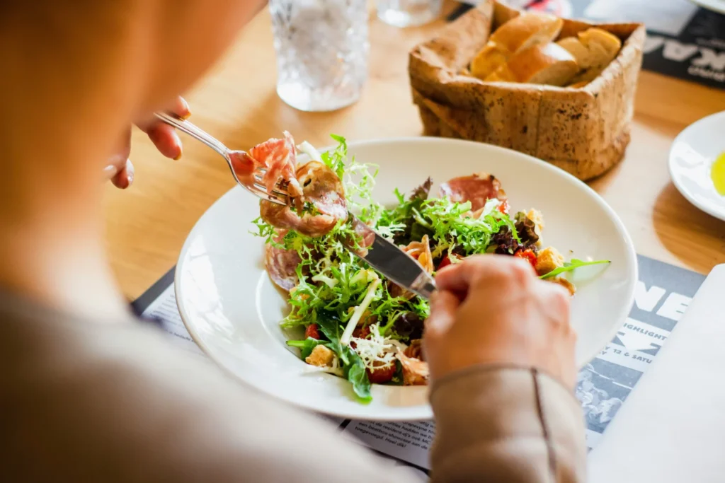 Person enjoying a fresh, healthy salad with prosciutto and greens at a restaurant, ideal for showcasing best restaurant marketing campaigns.