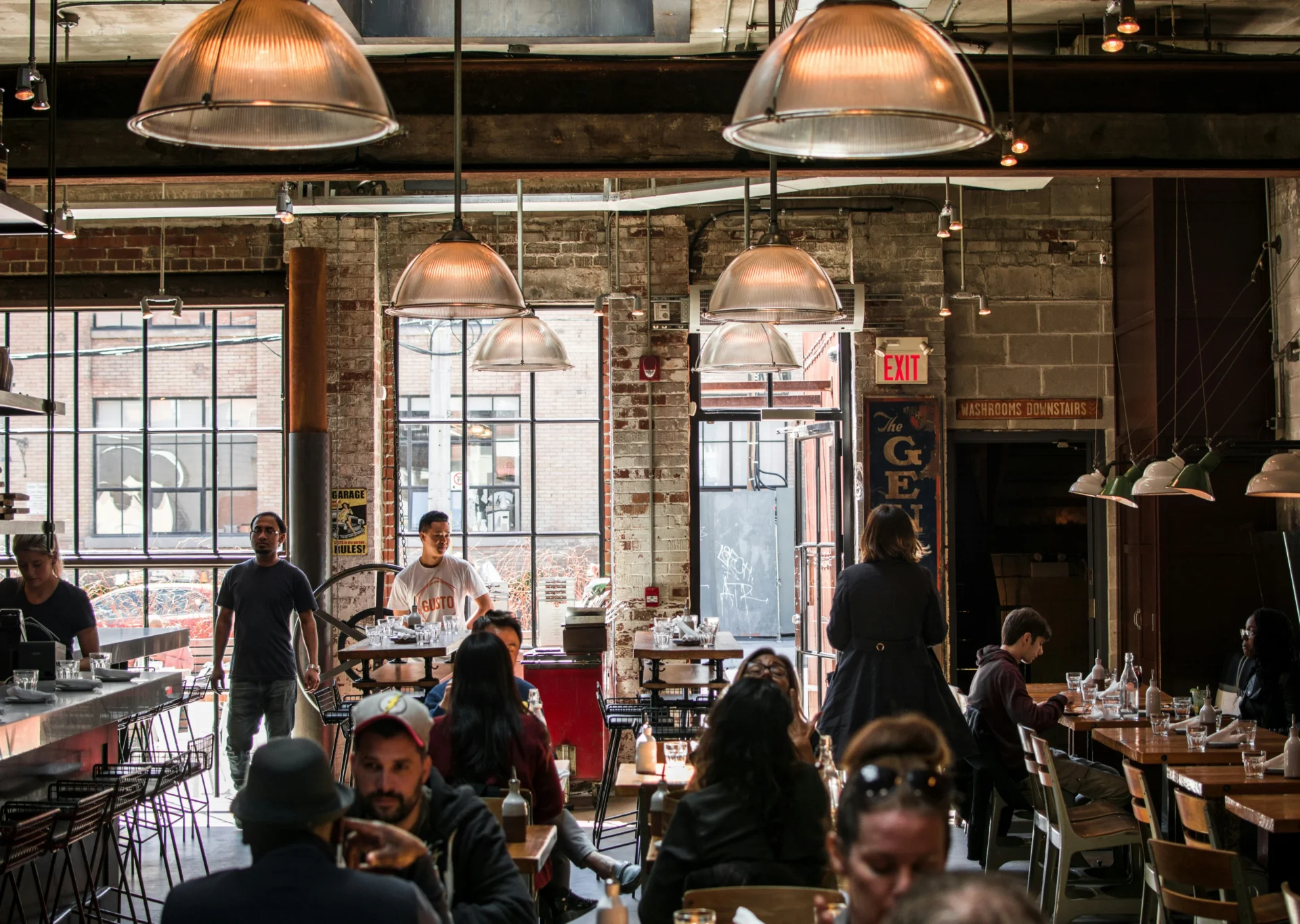 Bustling industrial-chic restaurant interior with diners, bar area, and exposed brick, showcasing a vibrant atmosphere for best restaurant marketing campaigns.