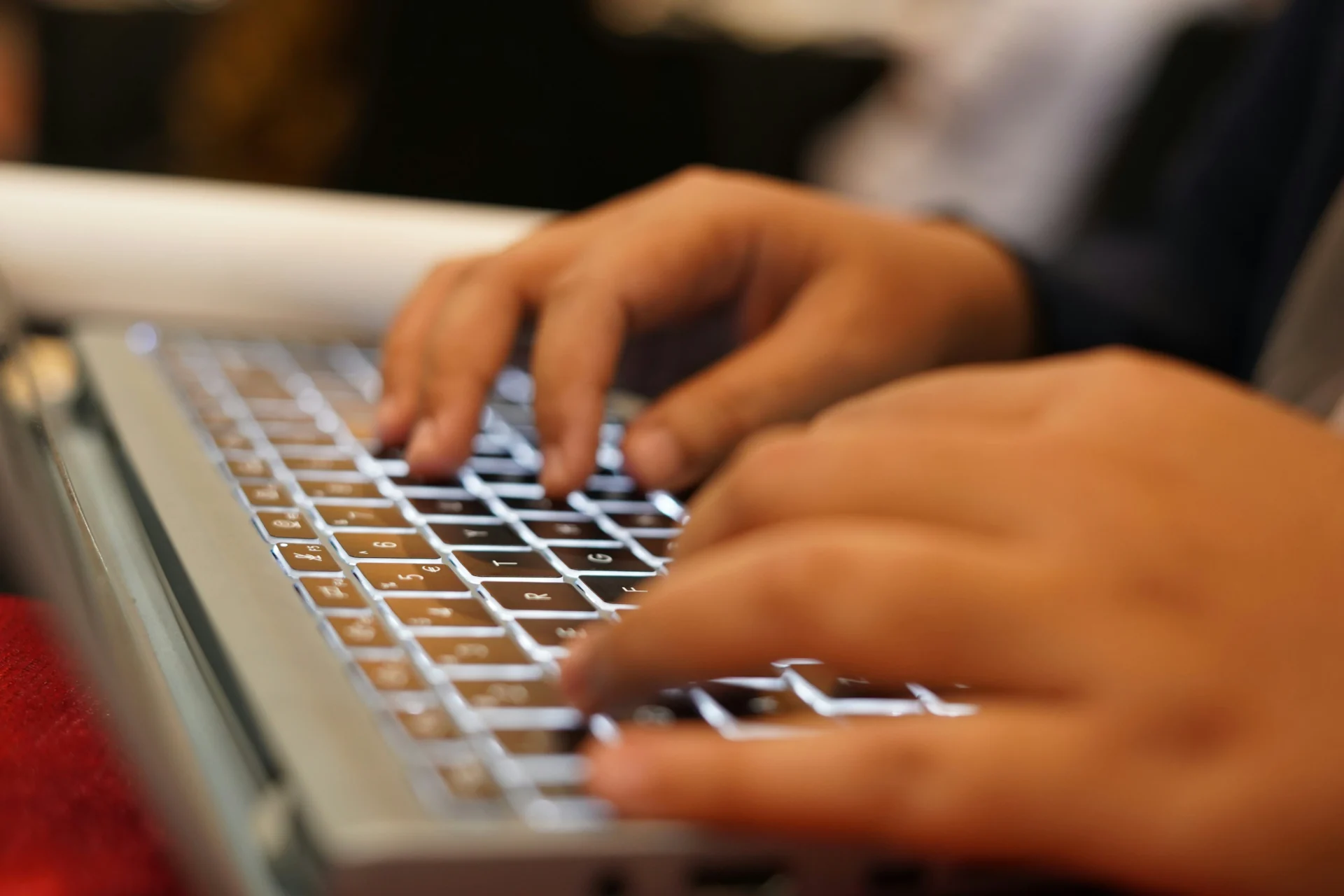 Hands typing on a laptop keyboard with glowing keys, focusing on informational keywords.
