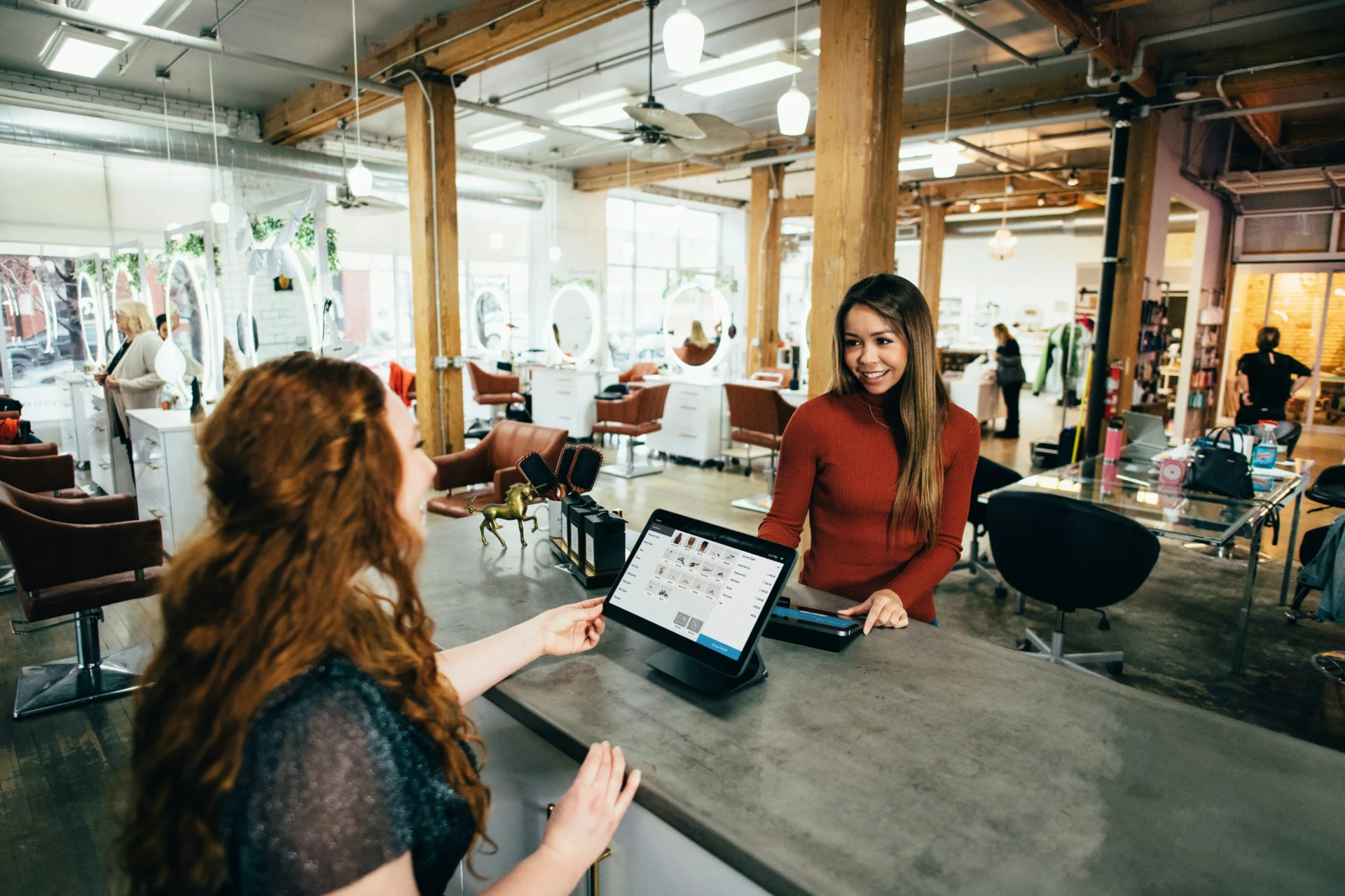 A salon or retail environment with a customer at the counter interacting with an employee at a point-of-sale system, illustrating how to increase customer engagement.