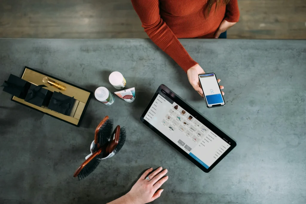 Overhead shot of a customer paying with a smartphone at a retail counter with various products, demonstrating how to increase customer engagement.