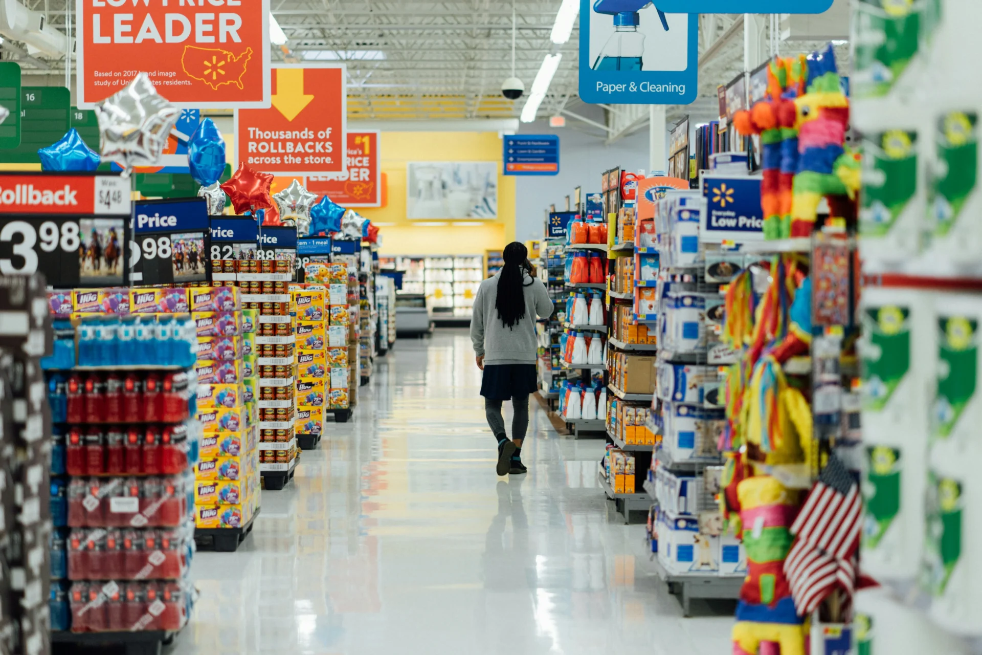 Person walking down a brightly lit supermarket aisle filled with CPG products, showcasing consumer goods and potential for CPG product innovation.