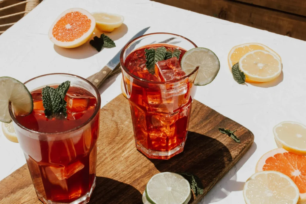 Two glasses of iced tea with citrus slices and mint, surrounded by fresh fruit, suitable for beverage marketing strategy visuals.