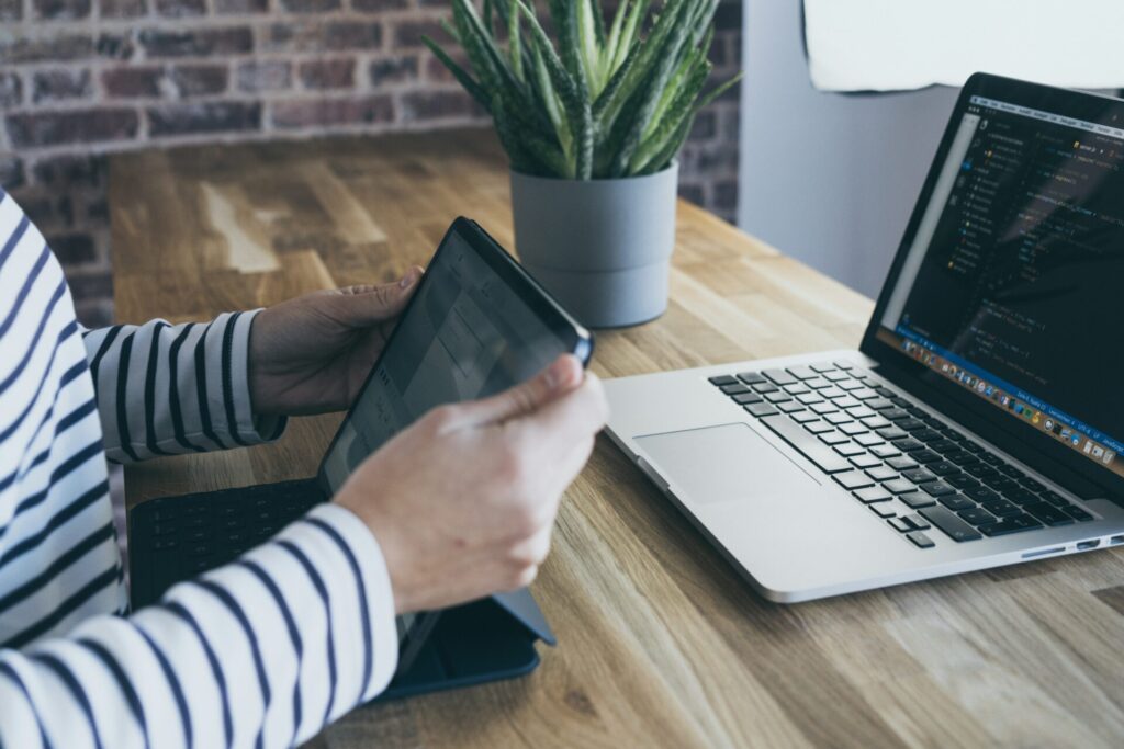 A person holding a tablet next to a laptop on a wooden desk with a plant, illustrating the tools used for international keyword research.