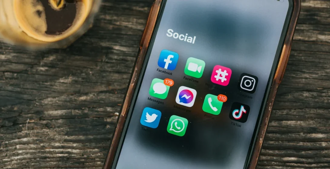Smartphone displaying social media app icons next to a coffee cup on a wooden table, representing engagement post ideas for social media.