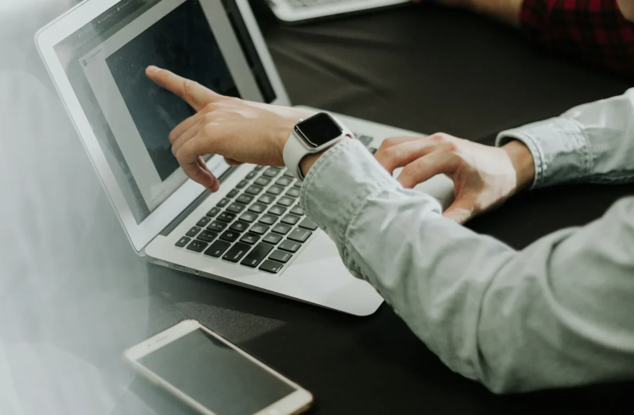 Person pointing at a laptop screen during a discussion, symbolizing analysis of what is a backlink profile.