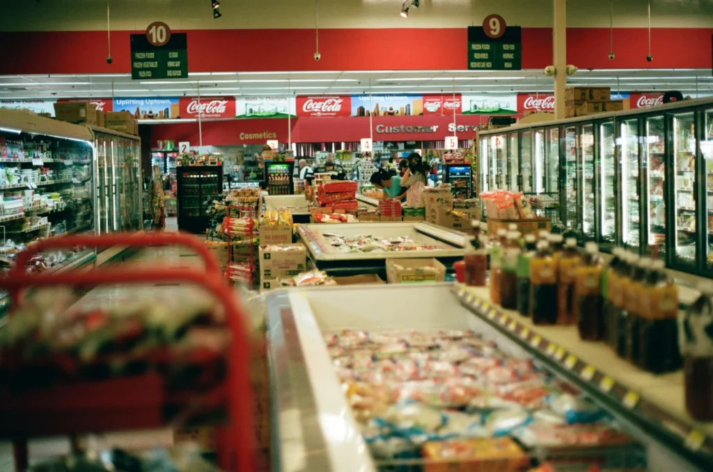 Wide view of a grocery store aisle with refrigerated sections, CPG beverage displays, and a customer service counter in the background.