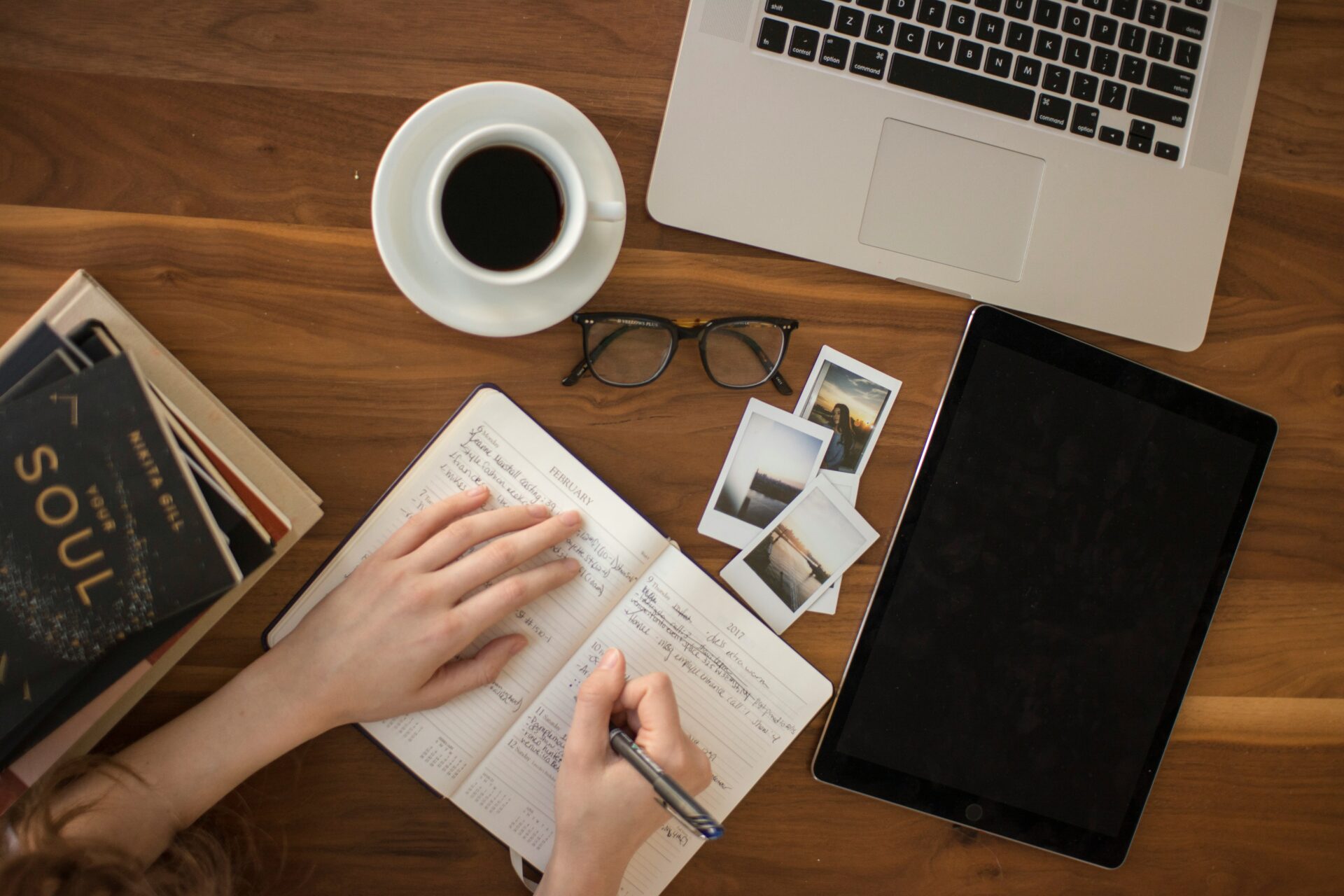 Overhead view of a person writing in a notebook next to a laptop, tablet, coffee, and glasses, suitable for a content marketing brief.