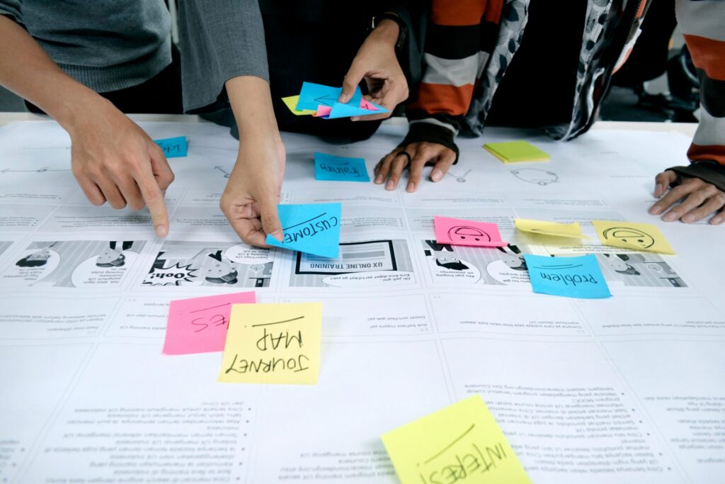 Multiple people collaborating on a large paper spread with sticky notes, engaged in a content mapping exercise.