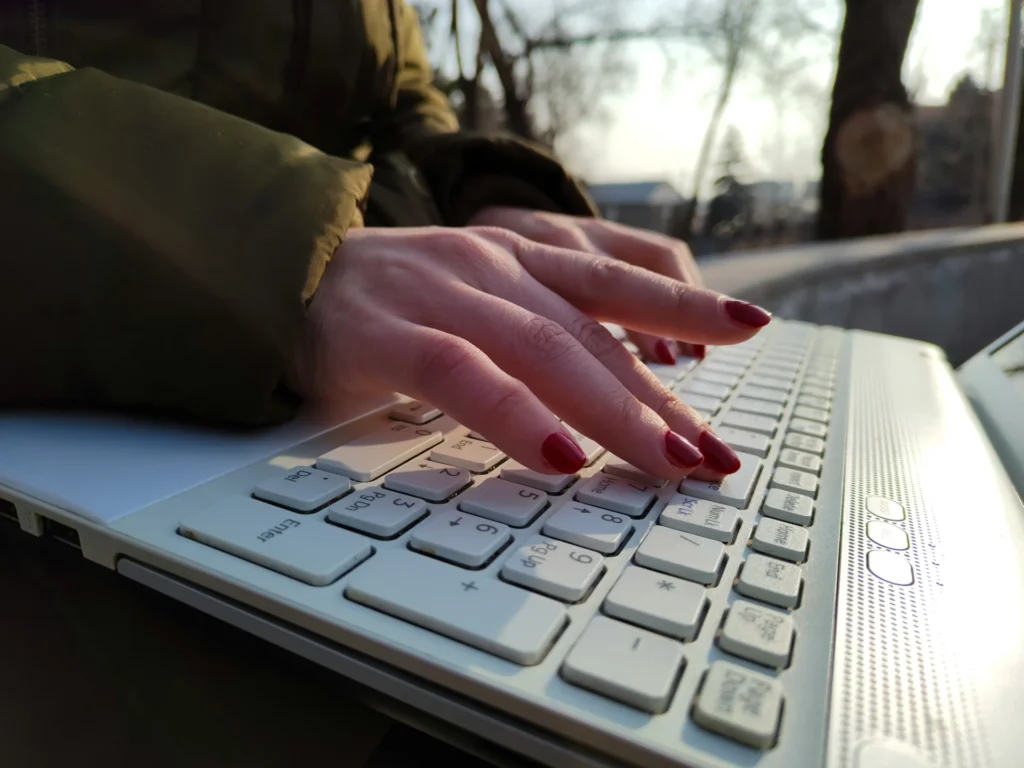 Hands with red nail polish typing on a white laptop keyboard outdoors, emphasizing the importance of backlinks.