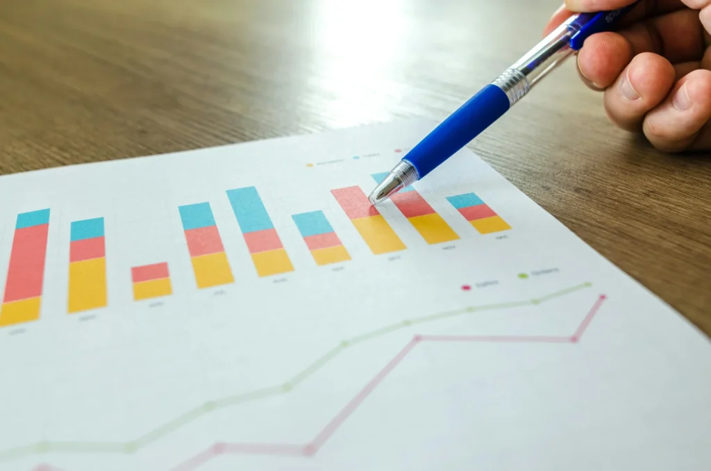A pen points to a bar graph on a paper, analyzing data to determine how can i get leads for my business.
