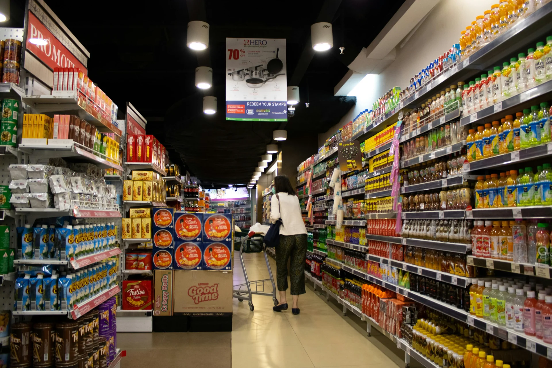 A person pushes a shopping cart down a supermarket aisle filled with a variety of products, representing a prime environment for consumer packaged goods analytics.