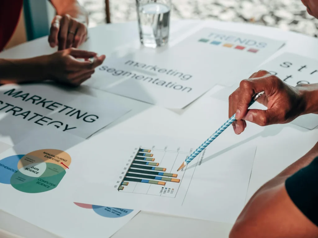 A person pointing to a bar graph on a desk with papers titled 'Marketing Strategy' and 'Marketing Segmentation,' outlining a plan for SEO for B2B strategy.