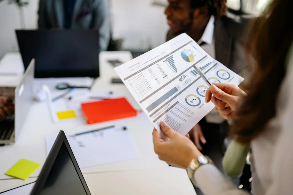 A person holds up a document filled with various charts and graphs, reviewing business data during a meeting.