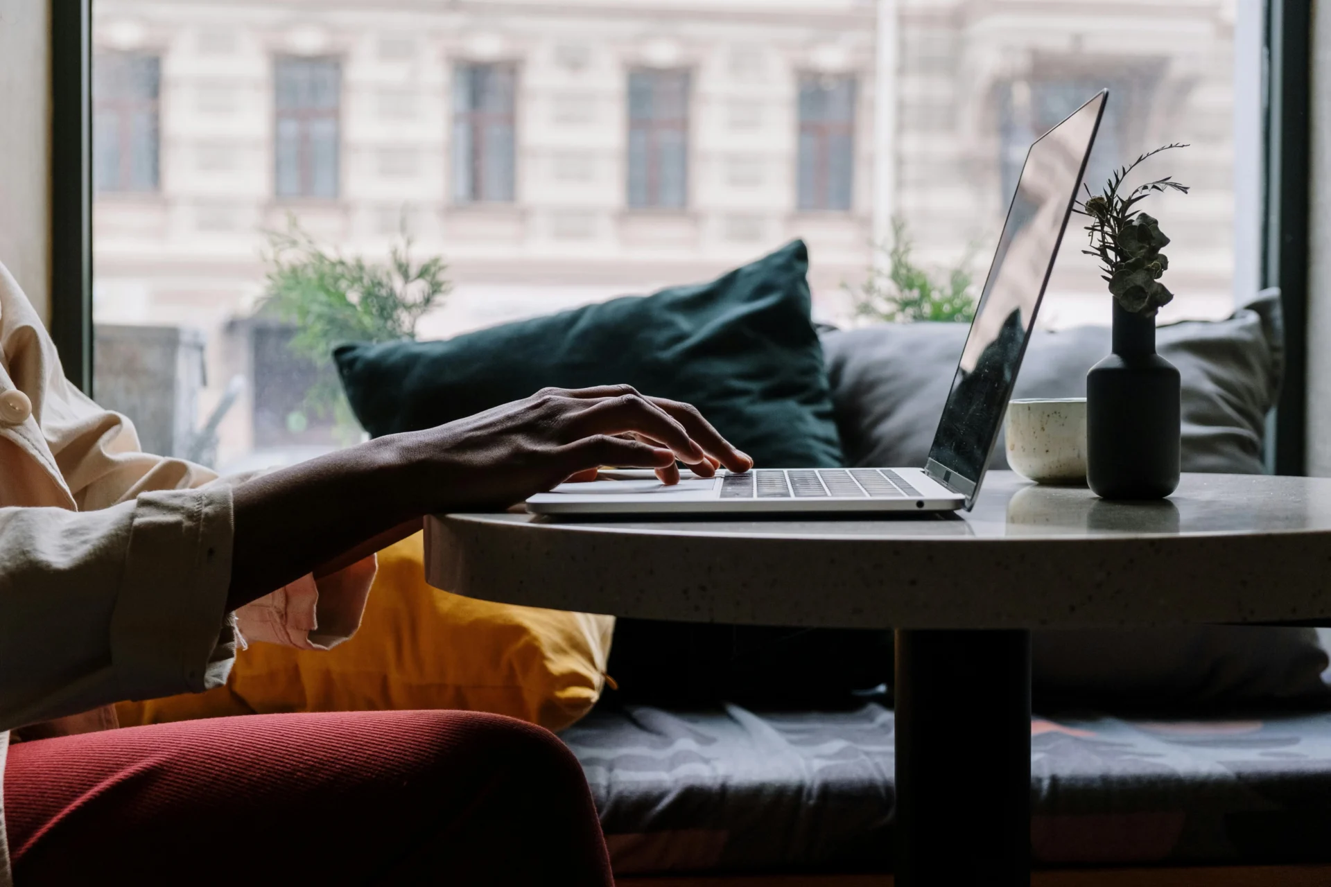 A person with a silver ring on their left index finger and multiple bracelets on their right wrist types on a laptop in a blurred office or cafe setting.