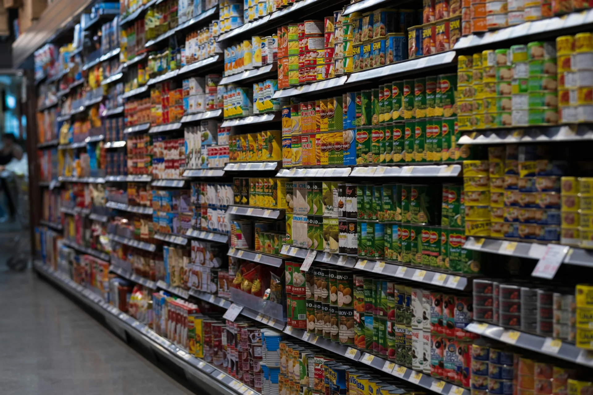 An aisle in a supermarket with shelves filled with colorful canned goods, showing a wide variety of food products.