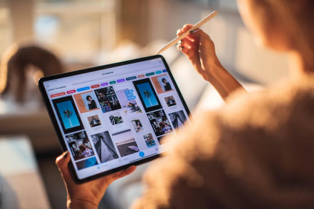 A person holds a tablet and uses a stylus to edit a template with various photos, with a screen displaying different design options.