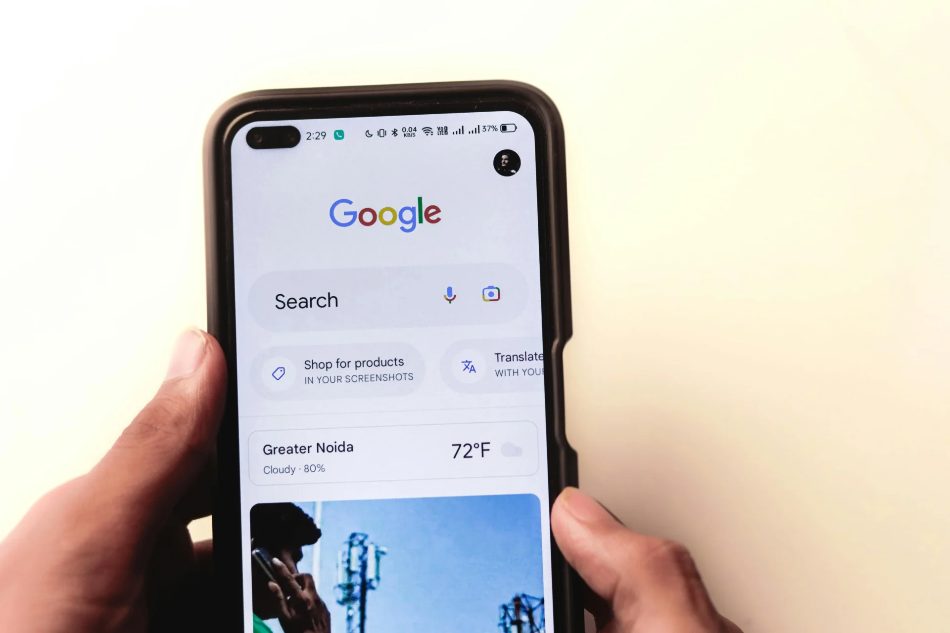 A hand holds a smartphone displaying the Google Search homepage, showing the search bar and weather for Greater Noida, to demonstrate the use of local search engines.