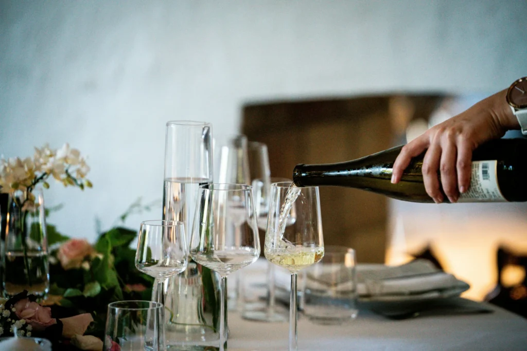 Hand pouring white wine into elegant wine glasses on a decorated dining table — a refined setup for wine marketing ideas.