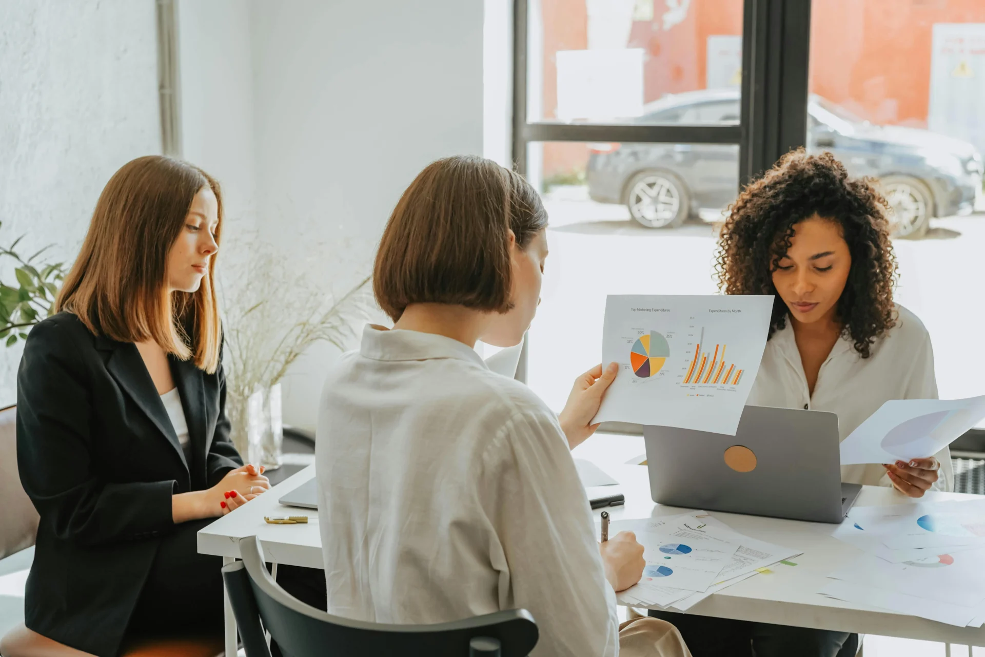 Three businesswomen reviewing charts and graphs during a meeting, discussing data analysis for SEO forecasting methods.