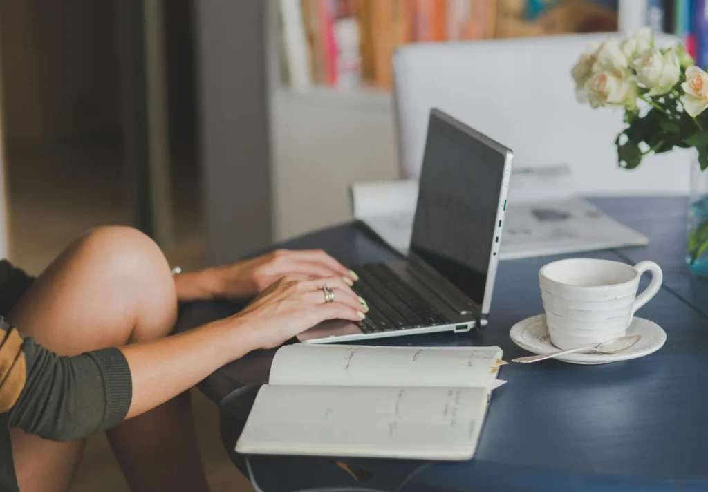 Person working on a laptop with notes and coffee — illustrating the difference between copywriting vs content writing.
