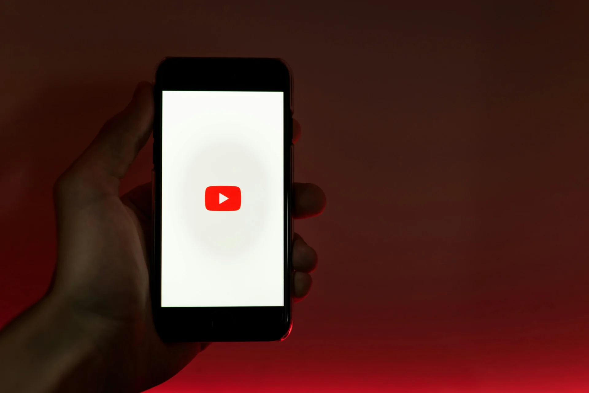 Hand holding a smartphone showing the YouTube logo against a red background — ideal for articles about YouTube content ideas for beginners.