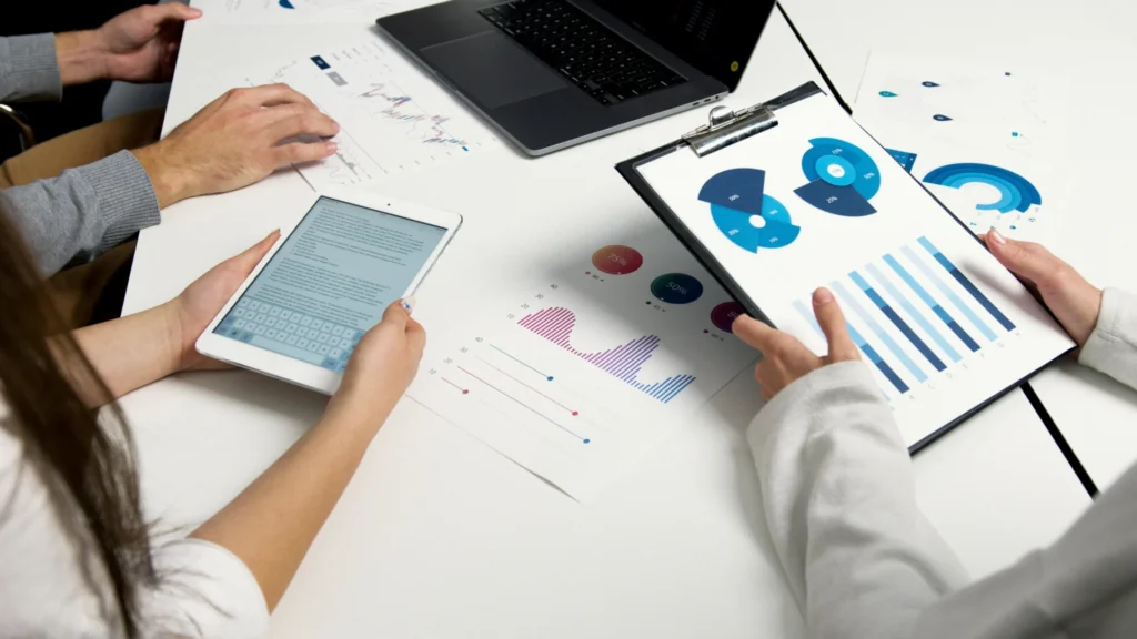 High-angle shot of three people reviewing data charts on a clipboard, papers, and a tablet, planning their strategy for what is B2B content marketing.