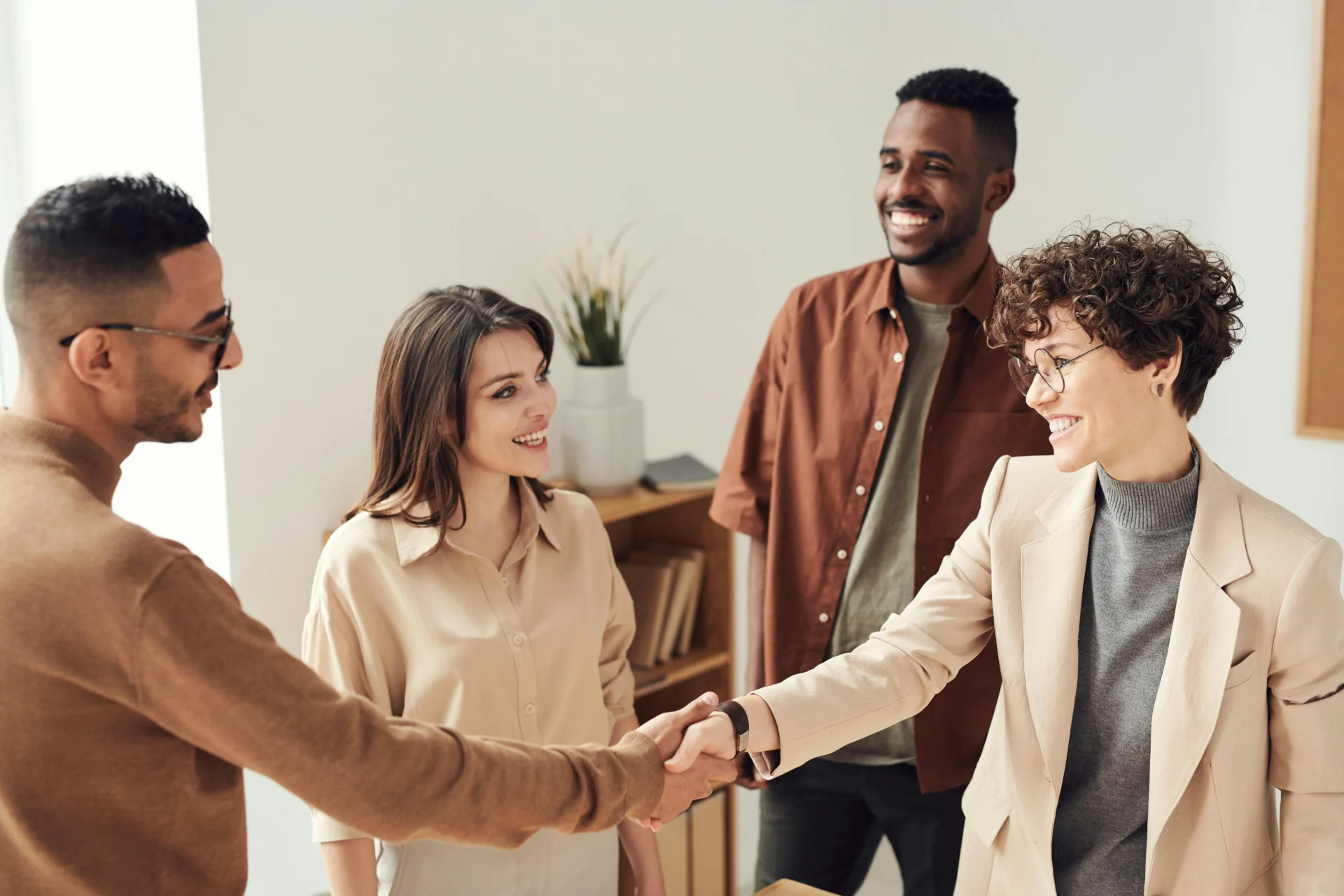 Four diverse professionals shaking hands after securing B2B leads, with two people smiling in the background.