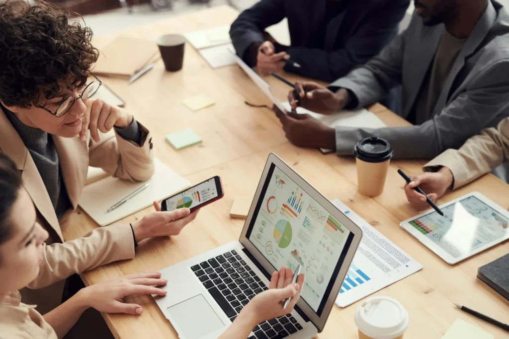 Diverse corporate team reviewing data on a laptop and mobile phone during a meeting focused on corporate digital transformation.