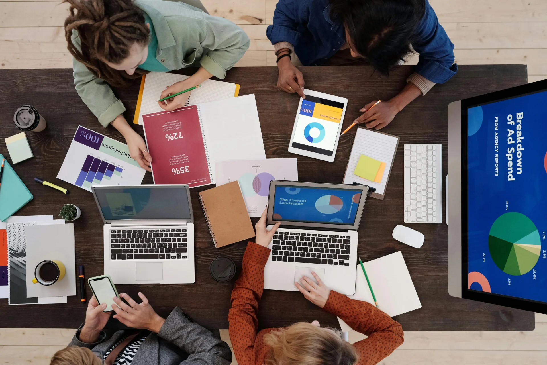 Overhead view of a diverse team analyzing complex data visualizations and reports on laptops, demonstrating strategy implementation for enterprise digital marketing solutions.
