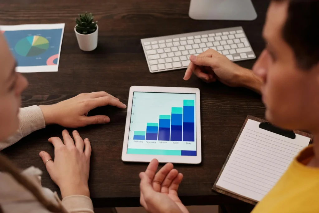 Two colleagues reviewing a tablet displaying a bar chart with consistent growth, discussing strategy for improving search engine positioning month-over-month.