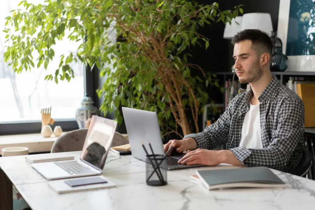 Young man working remotely on a laptop in a bright, green office setting, aiming for the goals of search engine optimization.