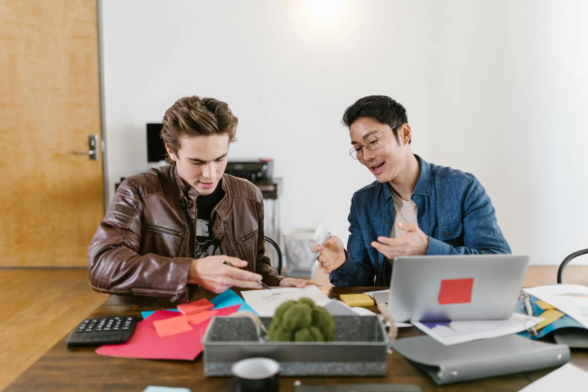 Two young professionals collaborate on startup branding strategy, reviewing sketches and papers on a desk filled with colorful sticky notes, demonstrating effective branding services for startups.