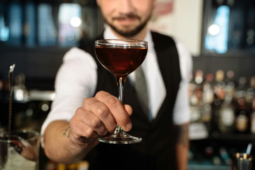Bartender holding up a perfectly mixed cocktail in a bar setting, representing the consumer side of a beverage industry analysis.