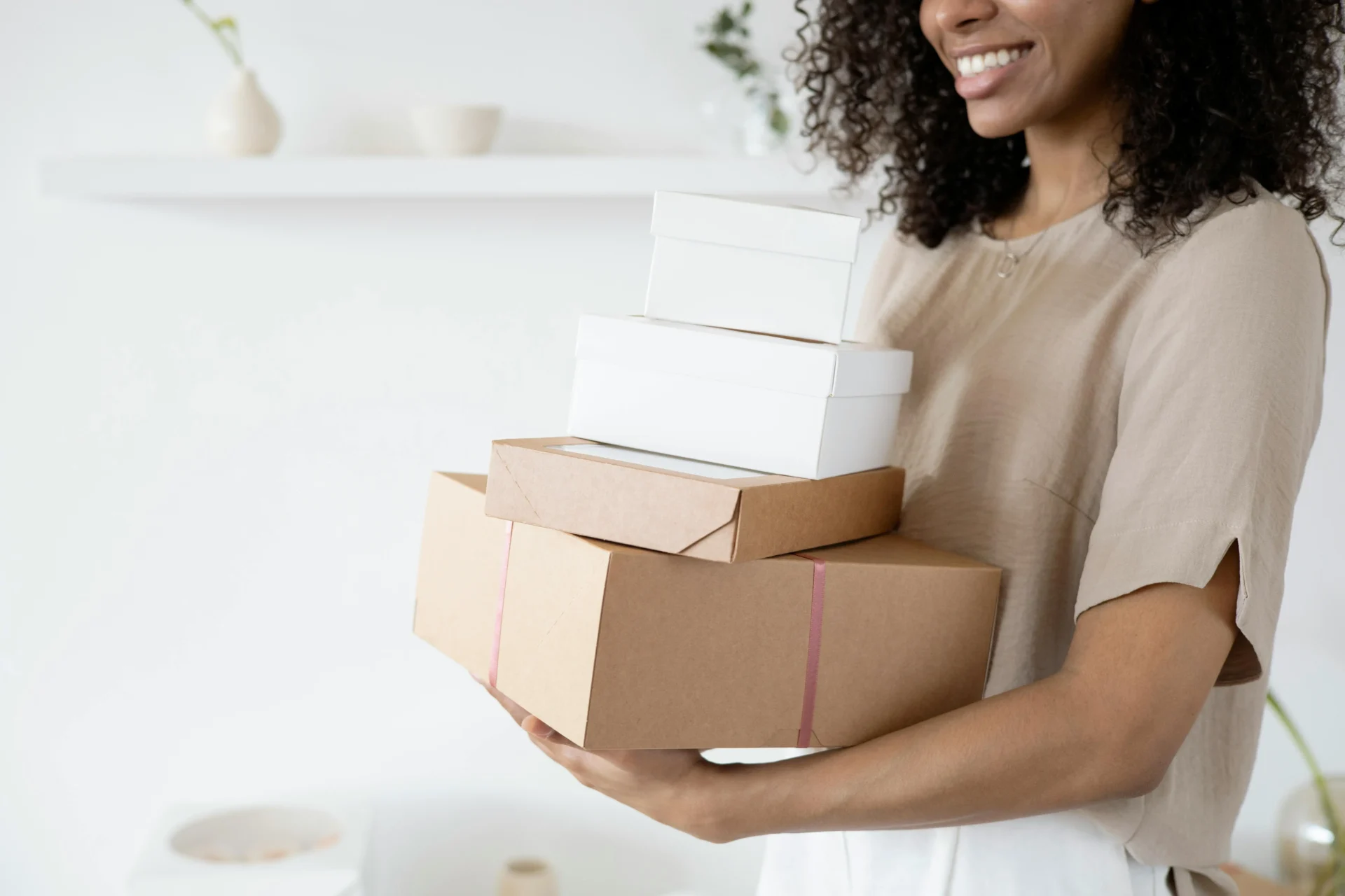 A smiling woman holding a stack of brown and white boxes, showcasing various options for sustainable CPG packaging design.