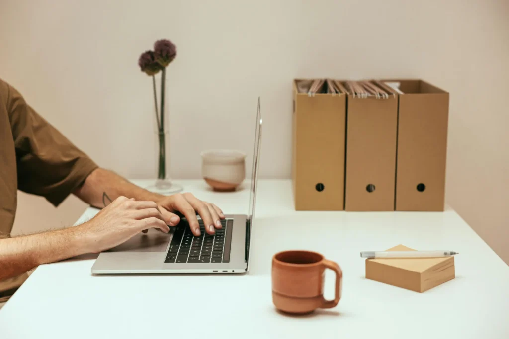Man typing on a silver laptop with file boxes nearby, learning what are semantic terms in SEO to organize digital archives.