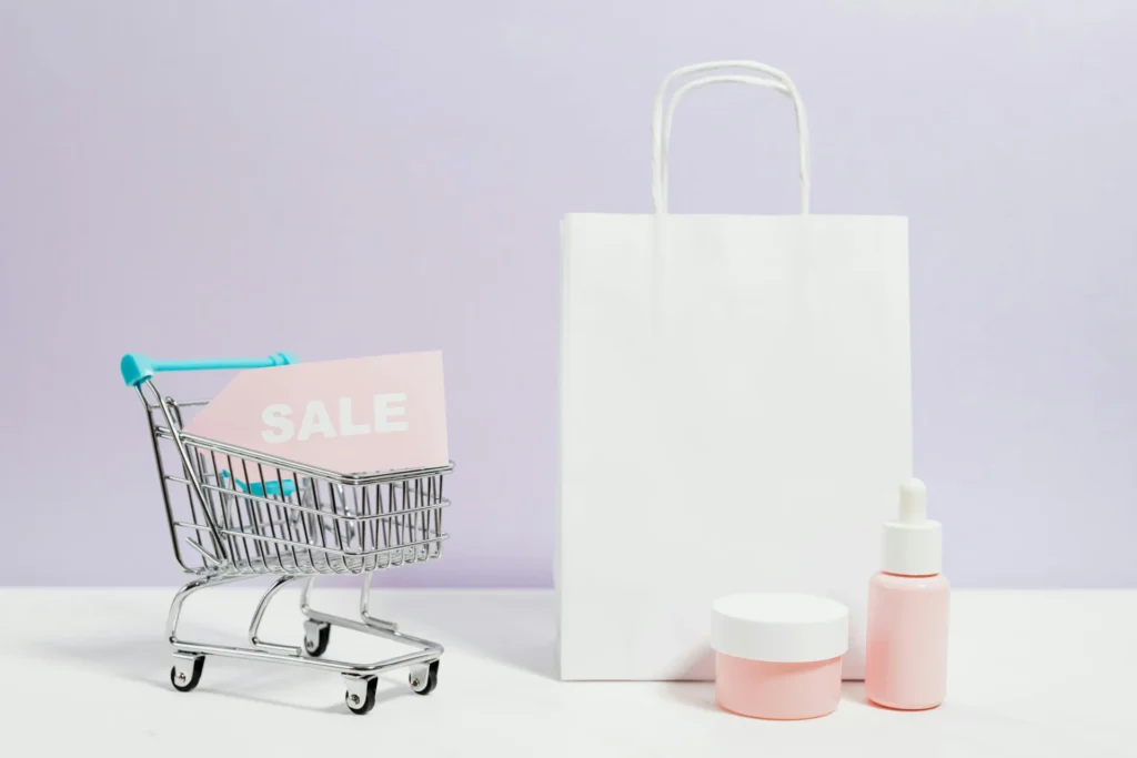 Small shopping cart with a 'SALE' sign, white shopping bag, and cosmetic bottles, emphasizing the role of CPG packaging design in promotional appeal.